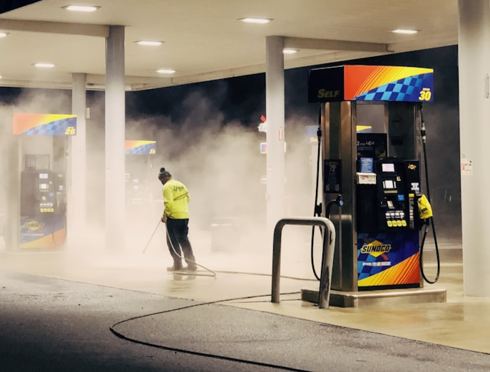 picture of a uniformed worker pressure washing a gas station parking lot