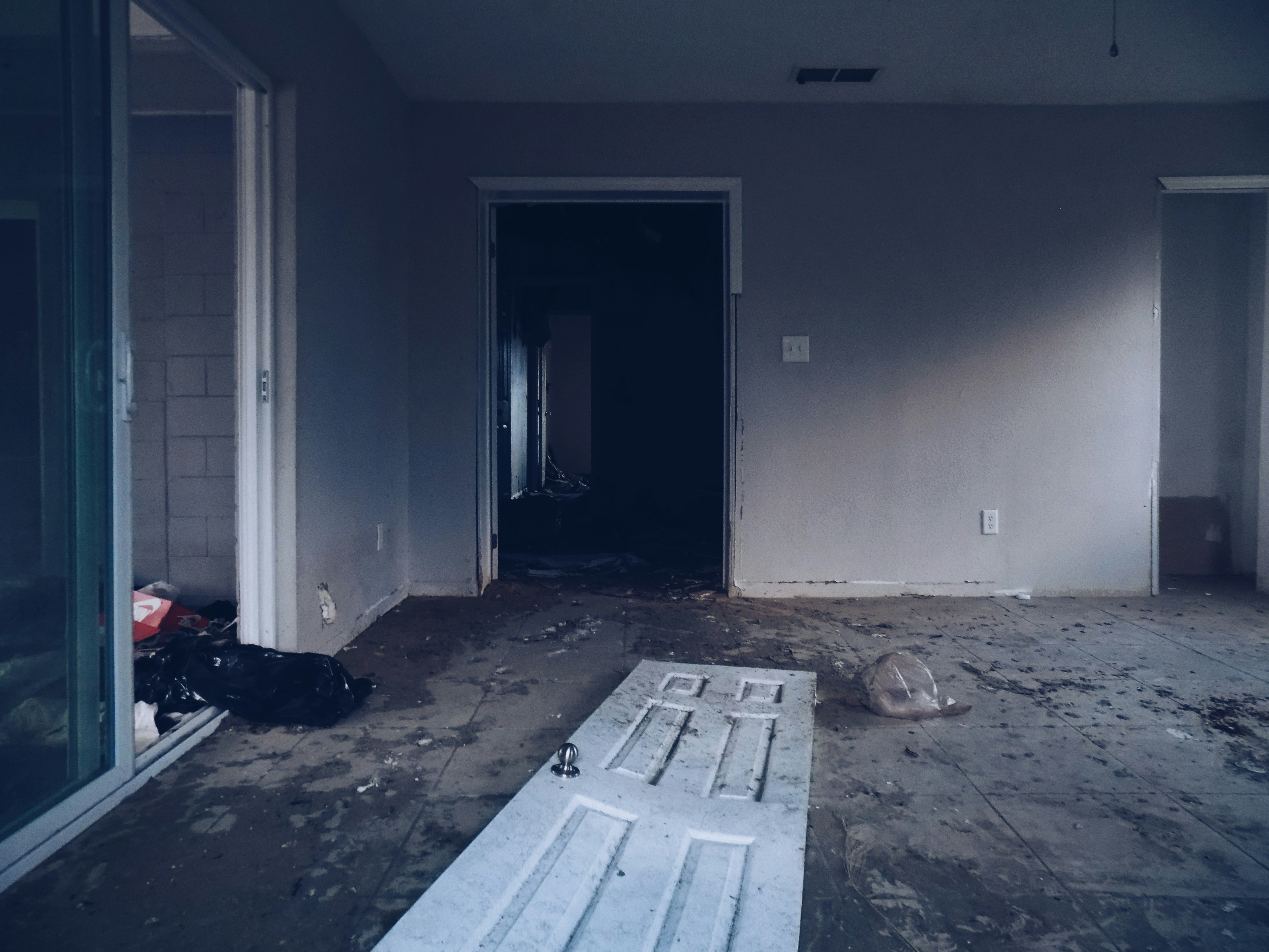 picture of empty house with damaged door on floor along with scattered debris.