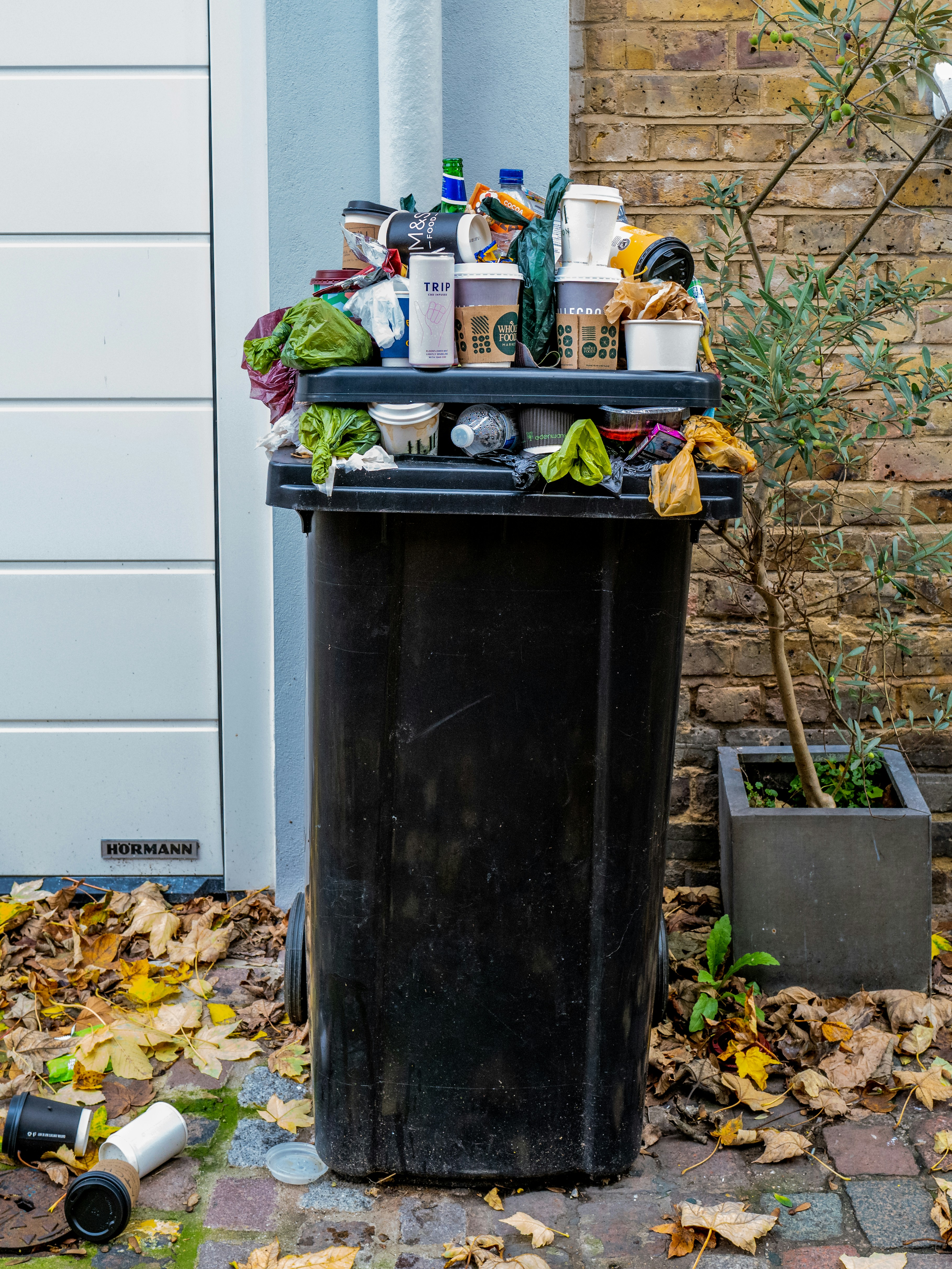 picture of scattered pieces of trash outside of an already full garbage can.